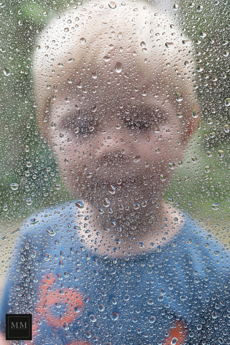 raindrops on a window with a boy behind enjoying rainy day portraits
