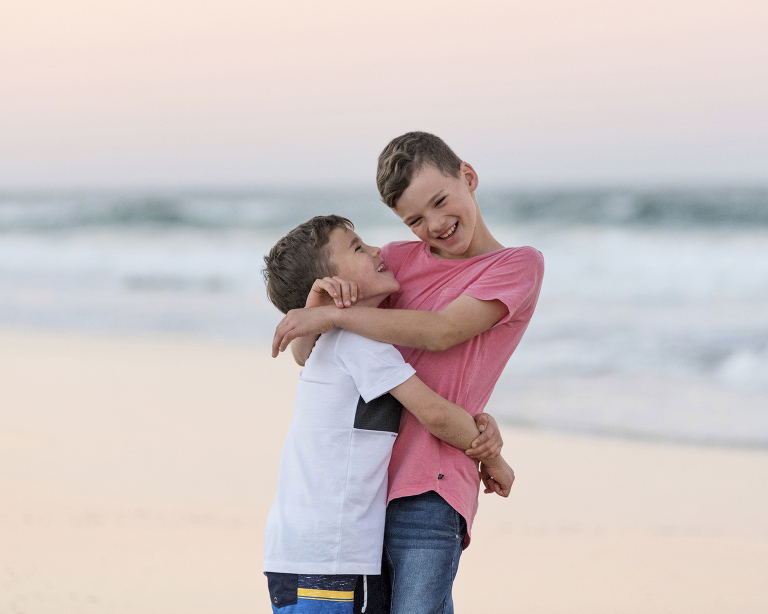 young brothers cuddling and laughing on the beach