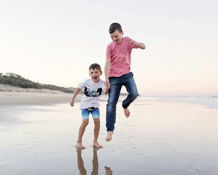 Noosa photographer capturing brothers jumping on the beach holding hands