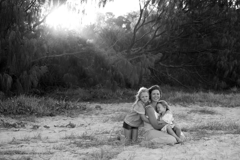mum and two young daughters at the beach cuddling