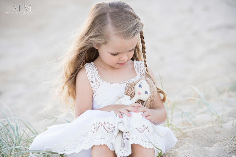 girl on beach cuddling doll
